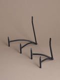 Two black iron plate display stands with curved support and matte finish against a taupe background