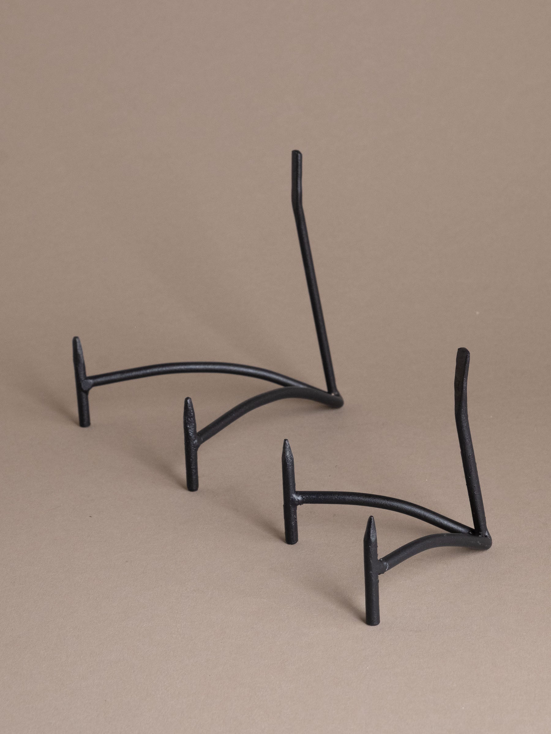 Two black iron plate display stands with curved support and matte finish against a taupe background