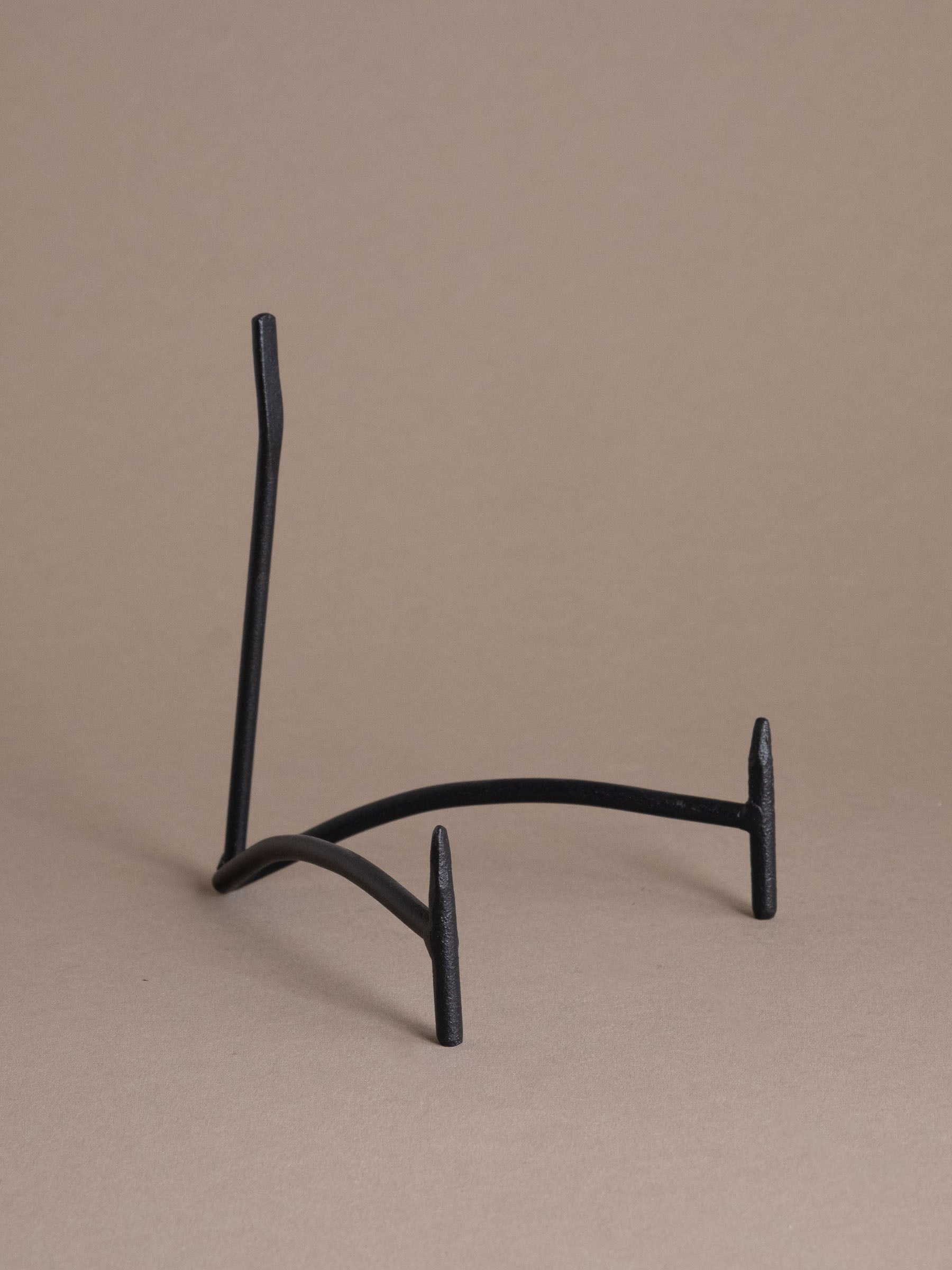 Front view of a black iron plate display stand with curved support and matte finish against a taupe background