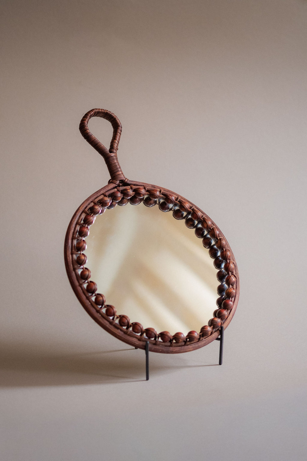 Angled side view of the round rattan wall mirror showing the shallow depth, beaded border, and loop handle.