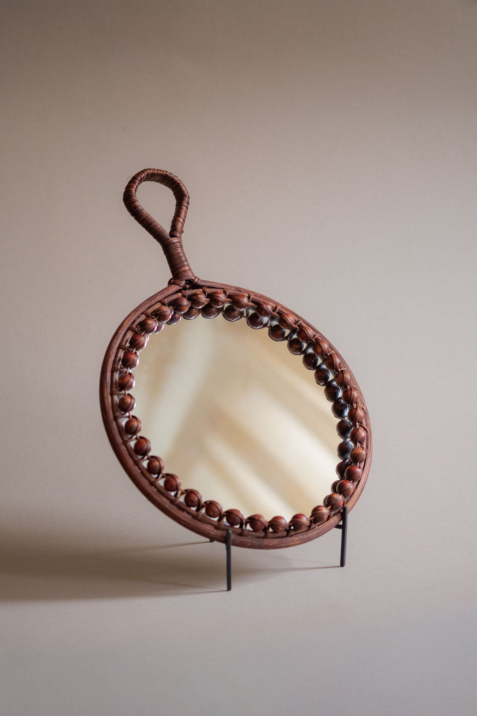 Angled side view of the round rattan wall mirror showing the shallow depth, beaded border, and loop handle.