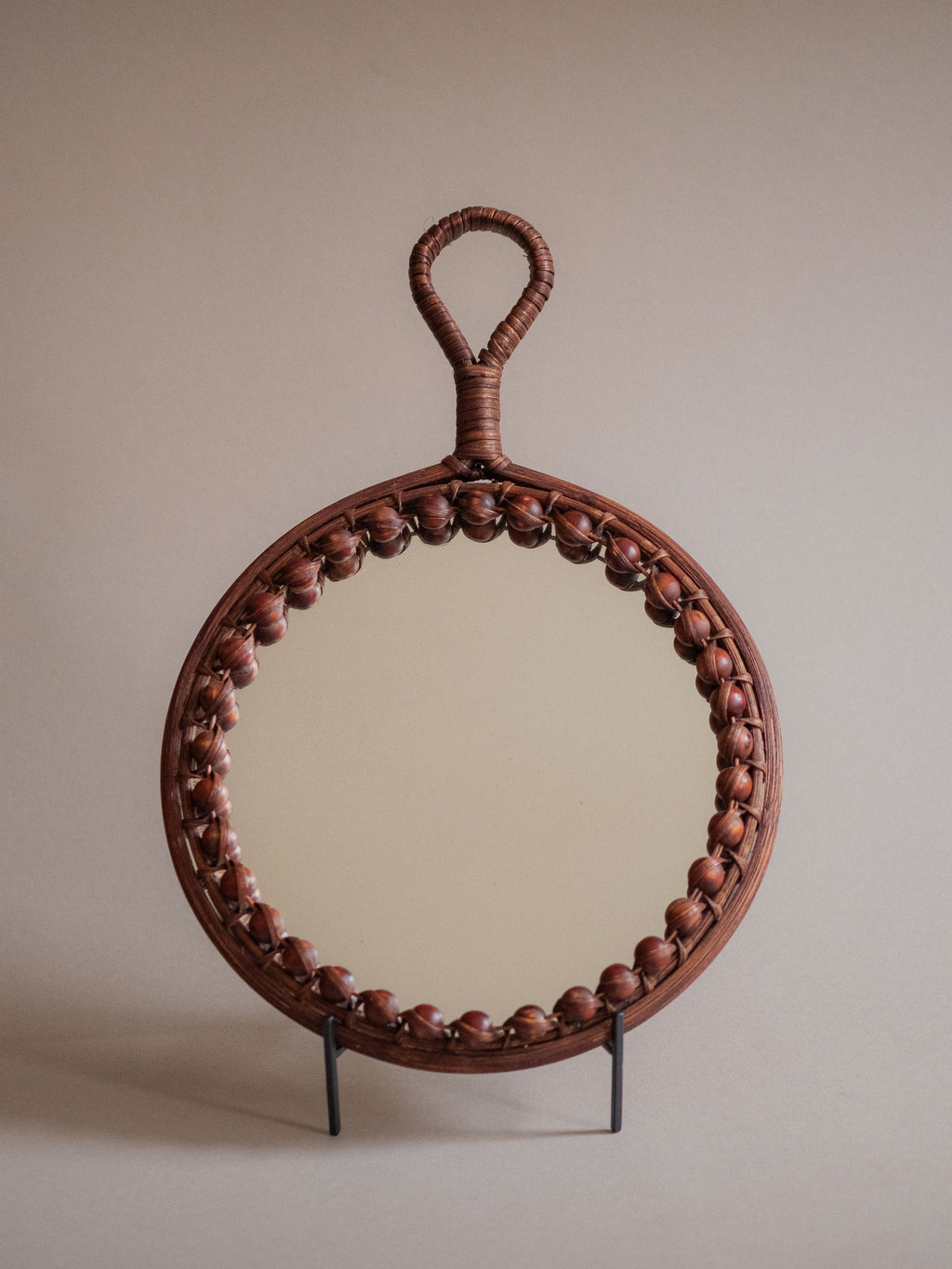 Full view of the round rattan wall mirror showing the wrapped loop handle and beaded frame detail.