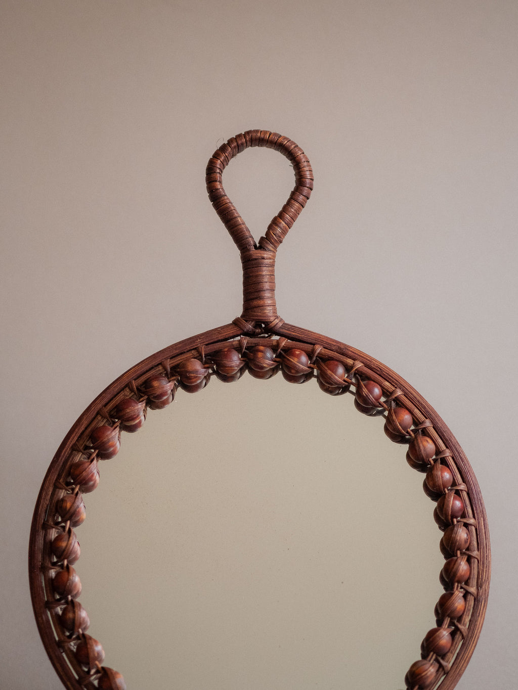 Upper front view of the round beaded rattan wall mirror against a neutral background.
