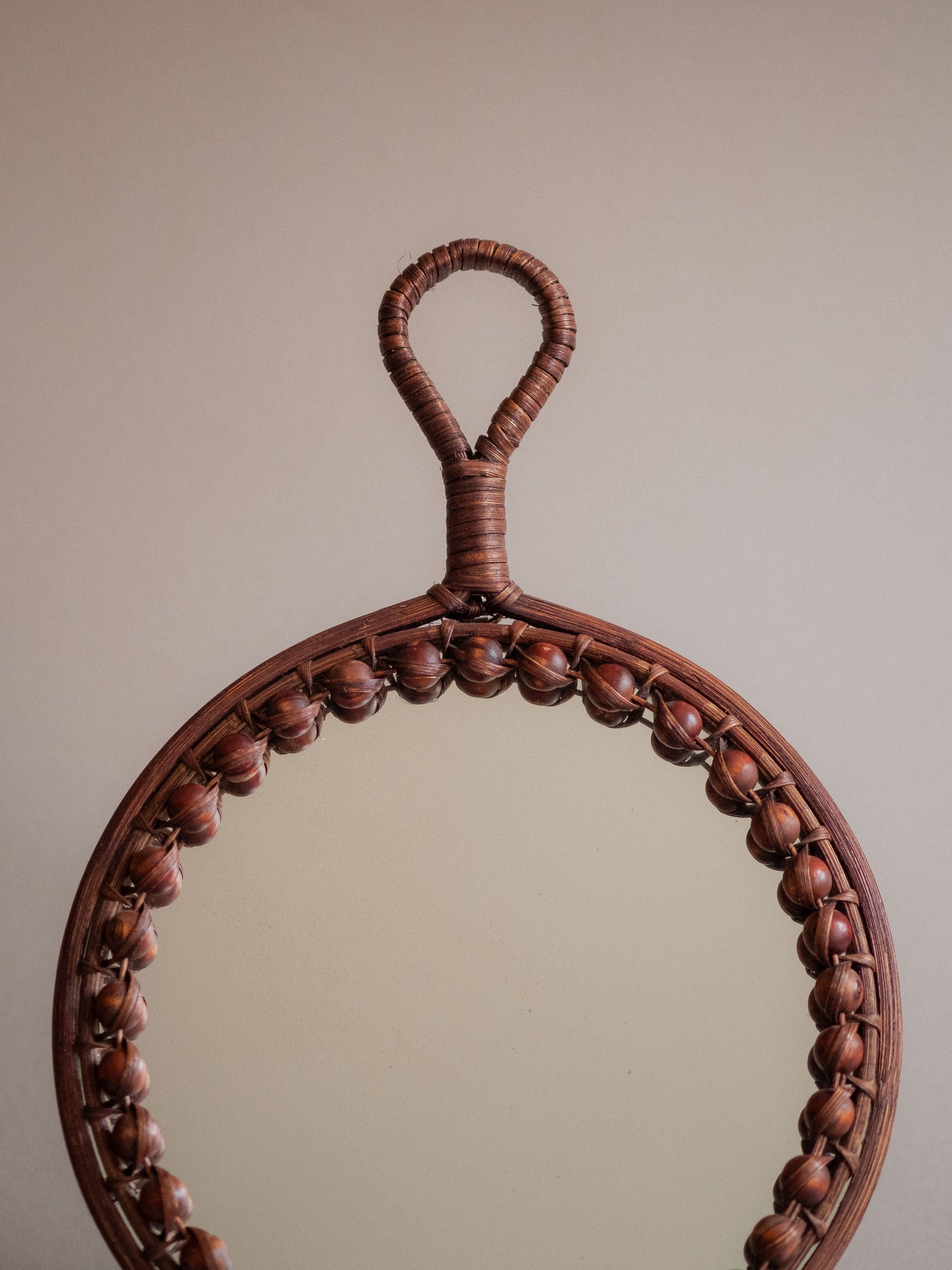 Upper front view of the round beaded rattan wall mirror against a neutral background.