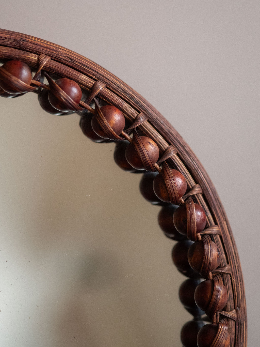 Detail of the upper edge of the round beaded rattan wall mirror with mirror plate and bead border.