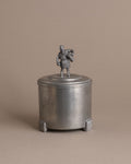 Front view of a small Savo Tinn pewter lidded box with a male figure finial and three ribbed feet.