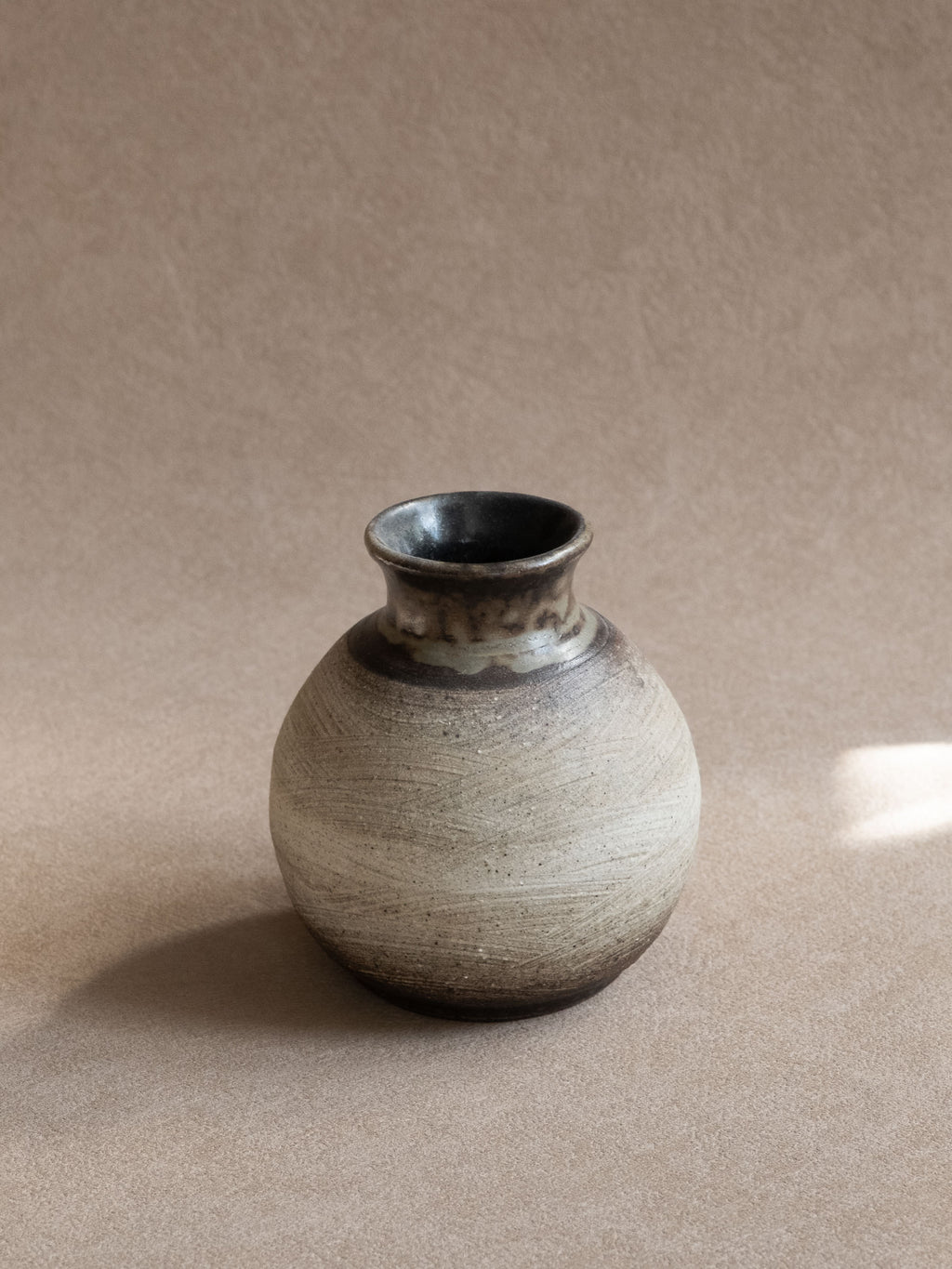 Small Japanese ceramic vase with rounded pale textured body and dark glazed neck.