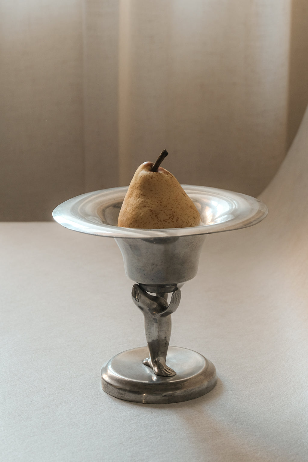 Pewter sea lion pedestal bowl by Dahlströms Tenn, Sweden, c. 1930s, shown holding a pear.