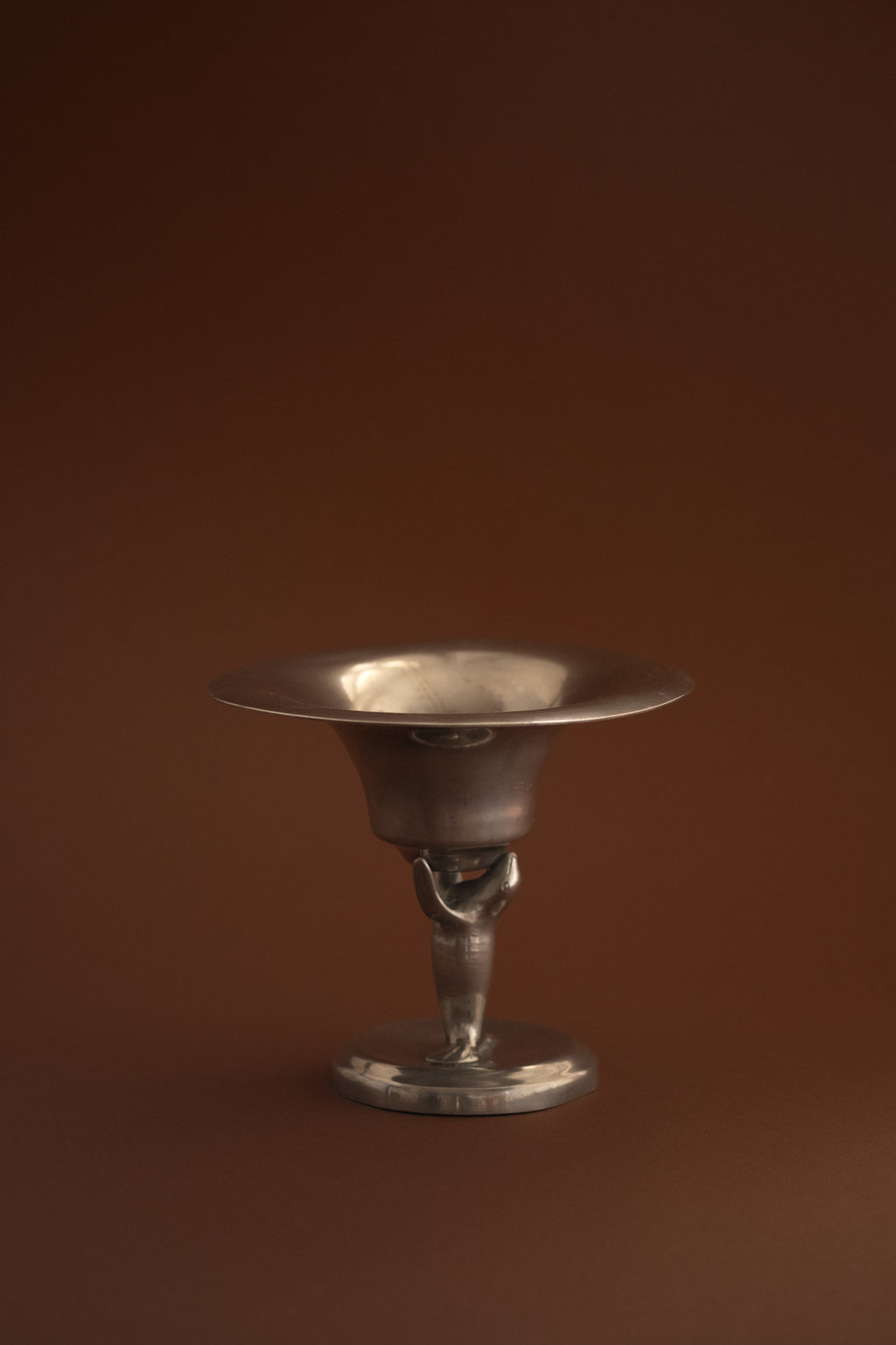 Side view of Dahlströms Tenn Swedish Grace pewter sea lion pedestal bowl on a dark background.
