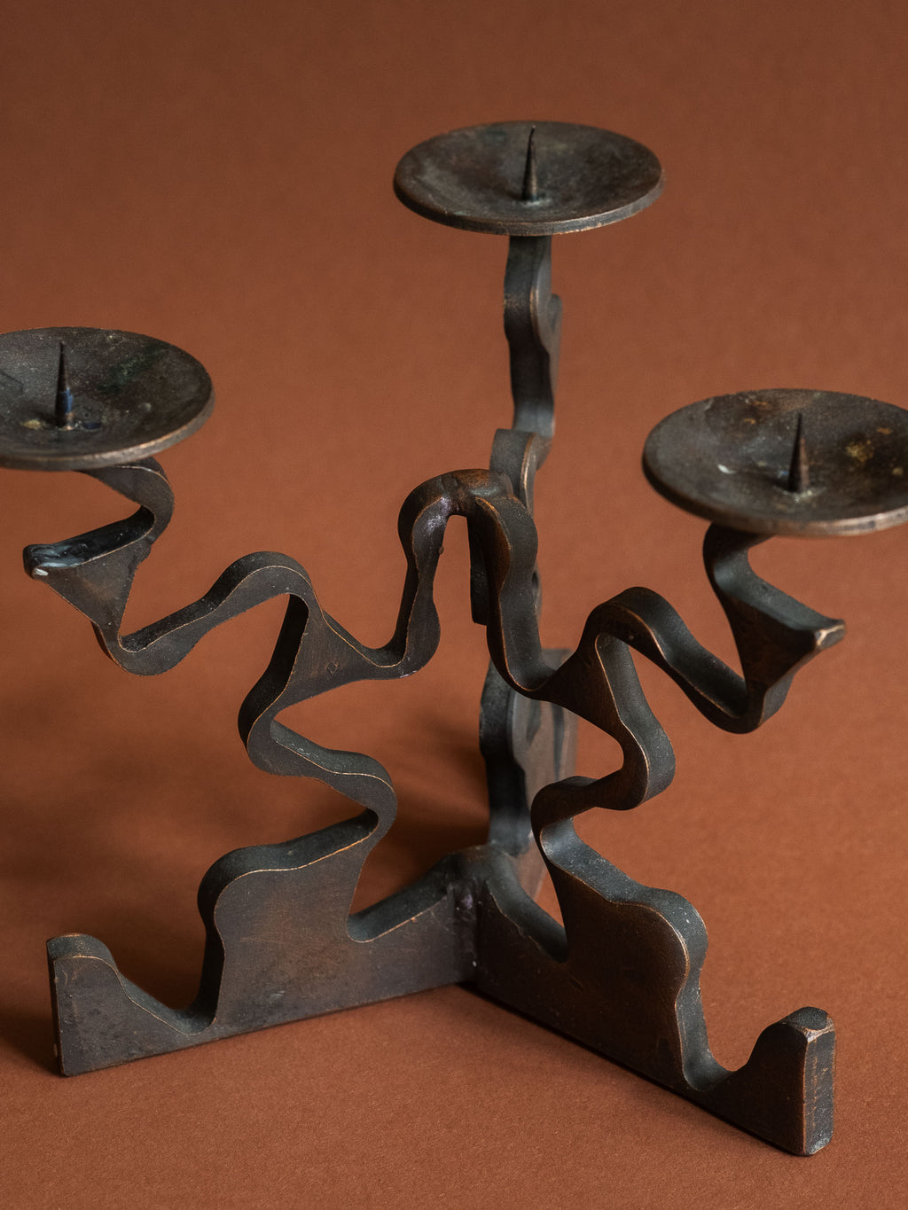 Closer three-quarter view of the candleholder showing the blackened surface, copper-bronze edge patina and age-related marks on the candle dishes.