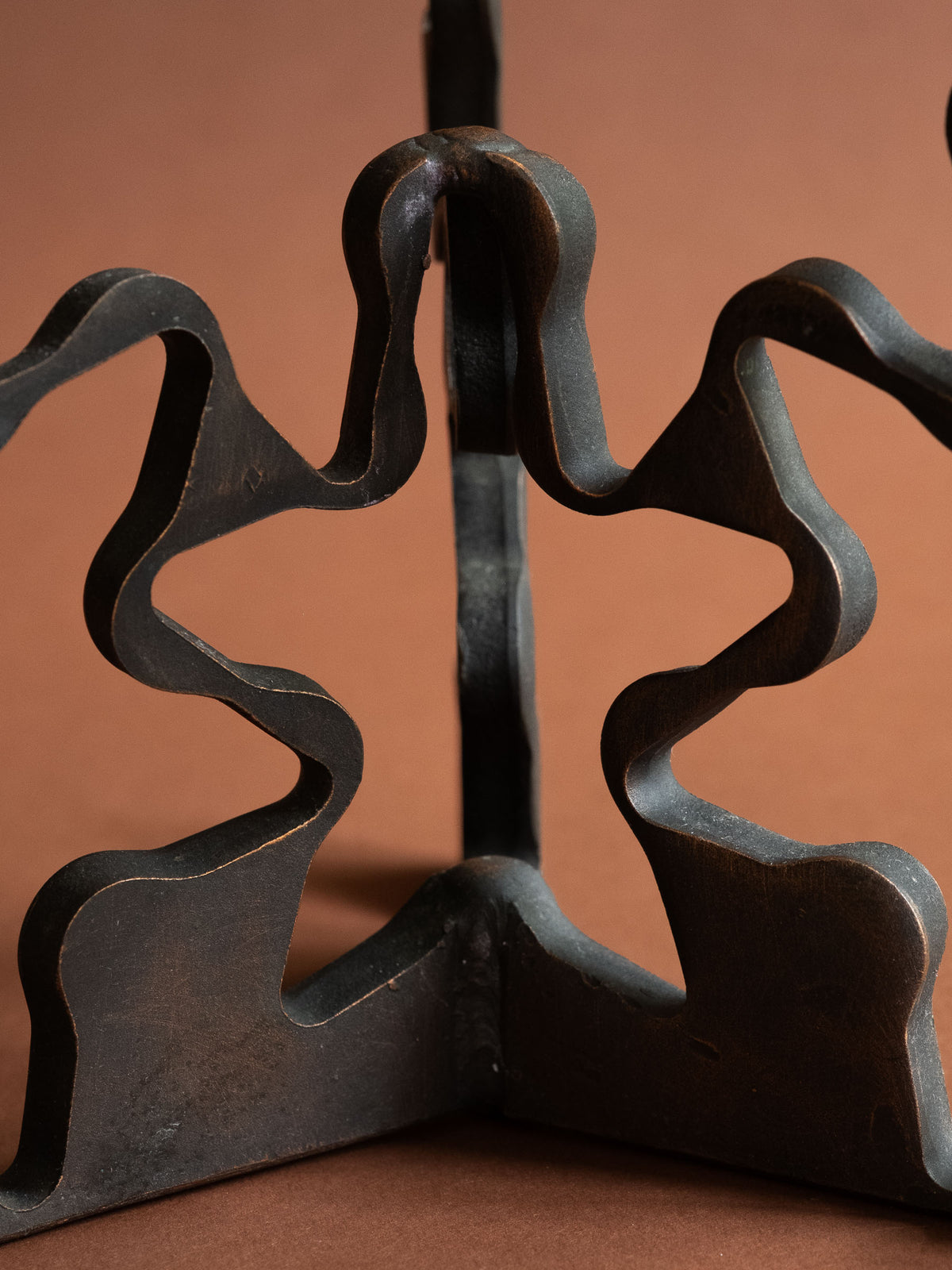 Close-up of the central looping forged iron structure and wave-cut base, highlighting warm copper-toned patina along the edges.