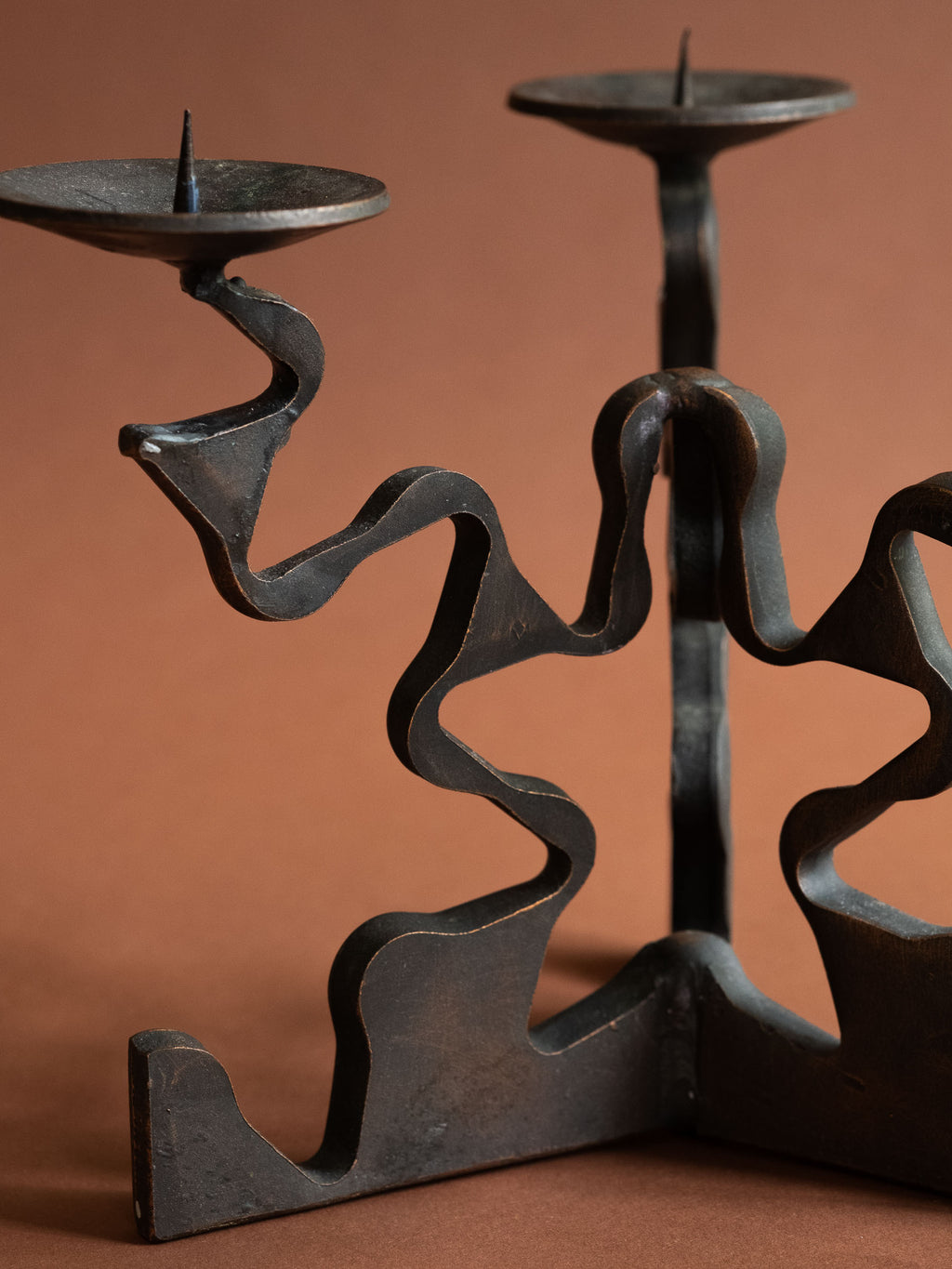 Close-up of one side of the three-arm candleholder showing a pricket dish, curling forged arm and warm surface wear along the edges.