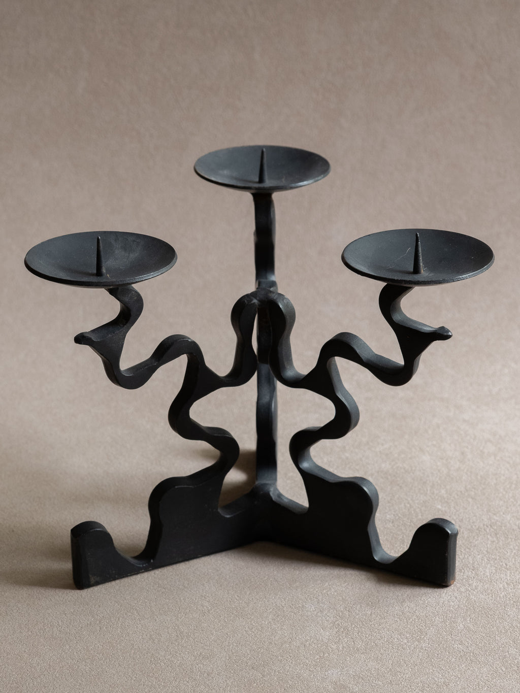 Closer front view of the forged iron three-arm candleholder, showing the pricket spikes, shallow dishes, curved arms, and black surface.