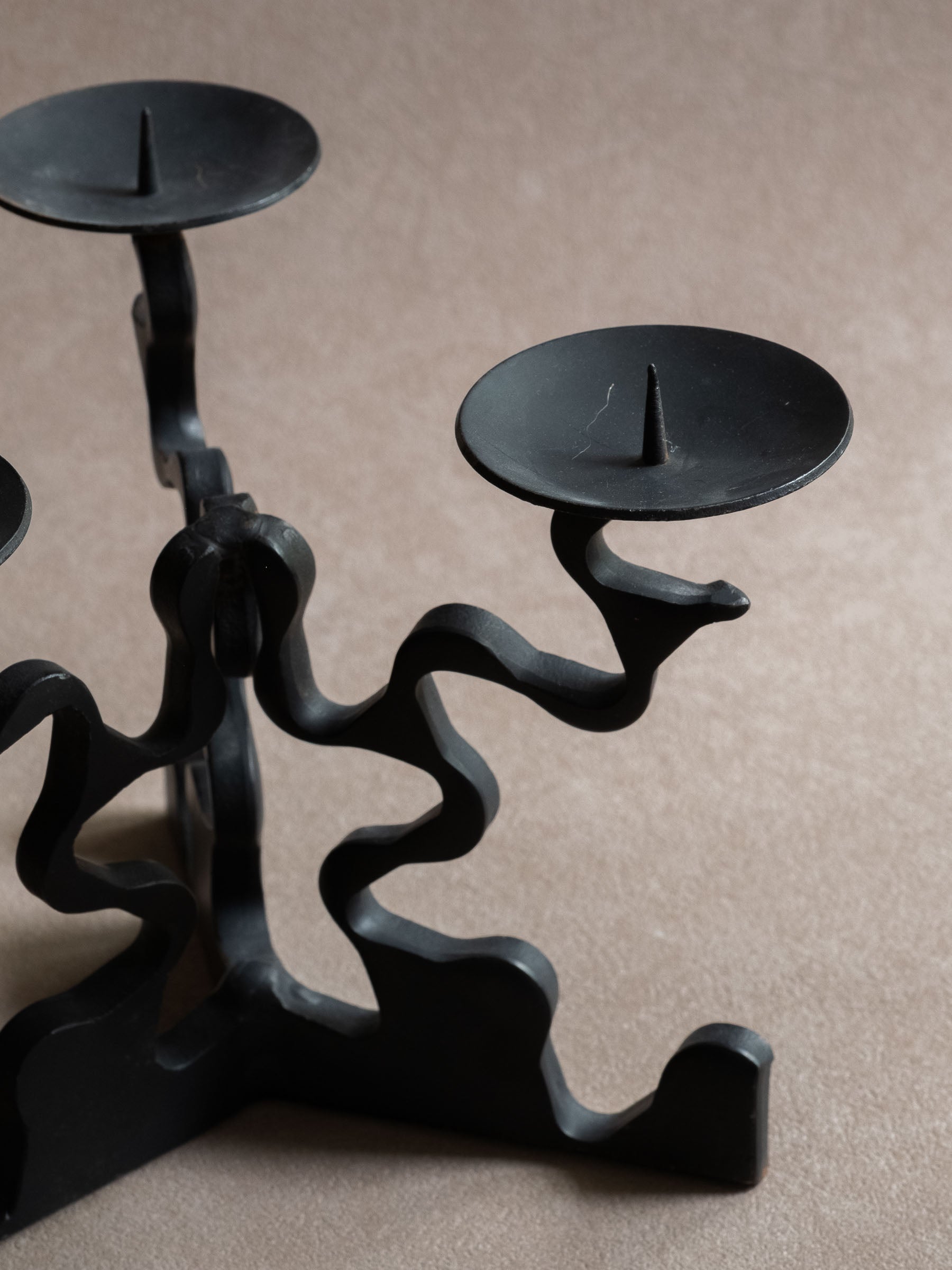 Detail view of the right candle dish and pricket spike, with visible light surface scratches and the curved forged iron arm below.