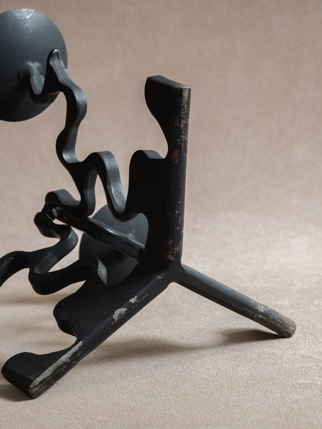 Detail view of the forged iron candleholder base and underside, showing scratches, exposed metal, blackened finish, and curved iron supports.
