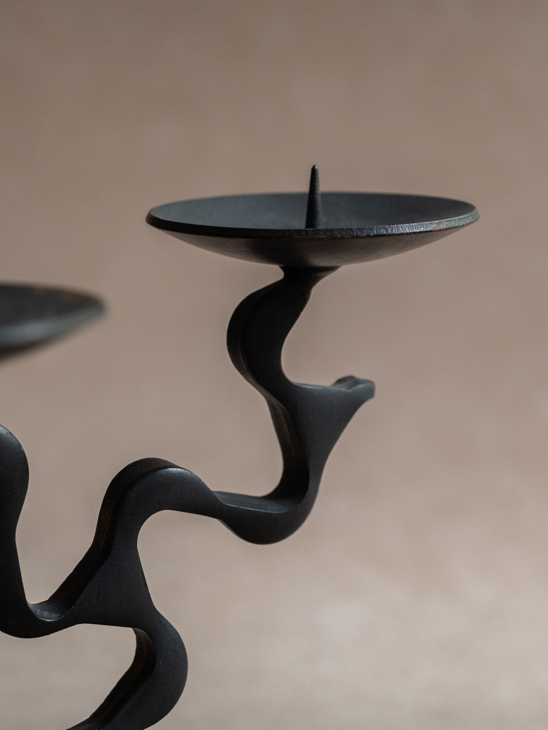 Close-up of one candle dish and pricket spike on the forged iron candleholder, with a blackened surface and curved supporting arm.