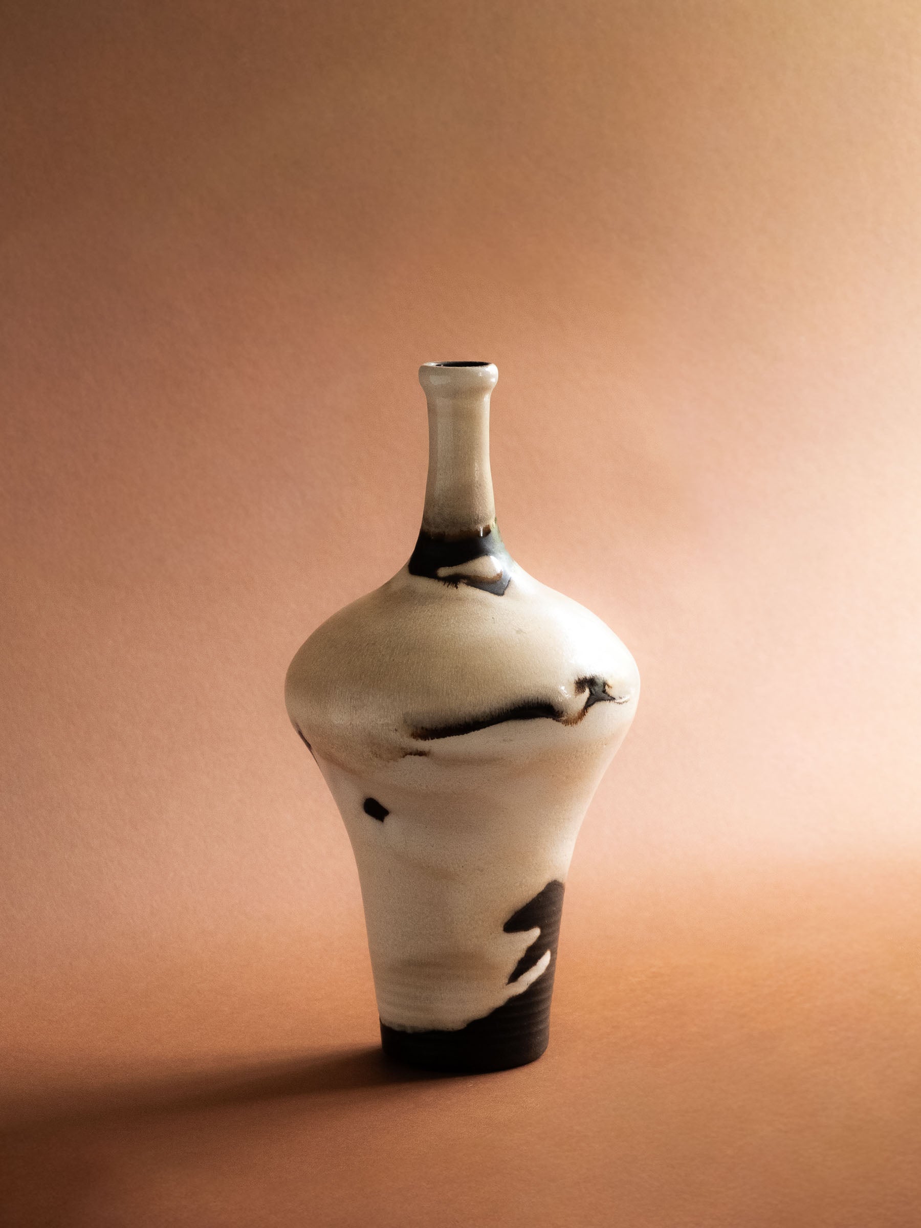 Hero view of the sculptural Kuch ceramic vase against a warm reddish background, showing its tall neck and rounded body.