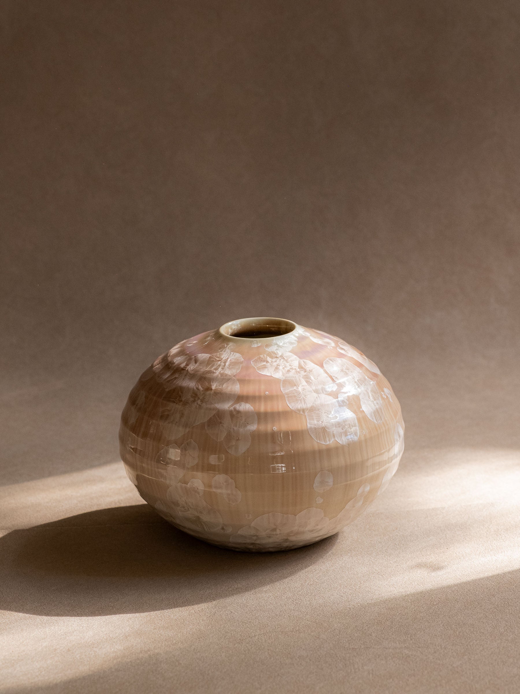 Full sunlit view of the rounded Tachikichi vase showing the crystalline glaze shifting between ivory, champagne and pale lilac.