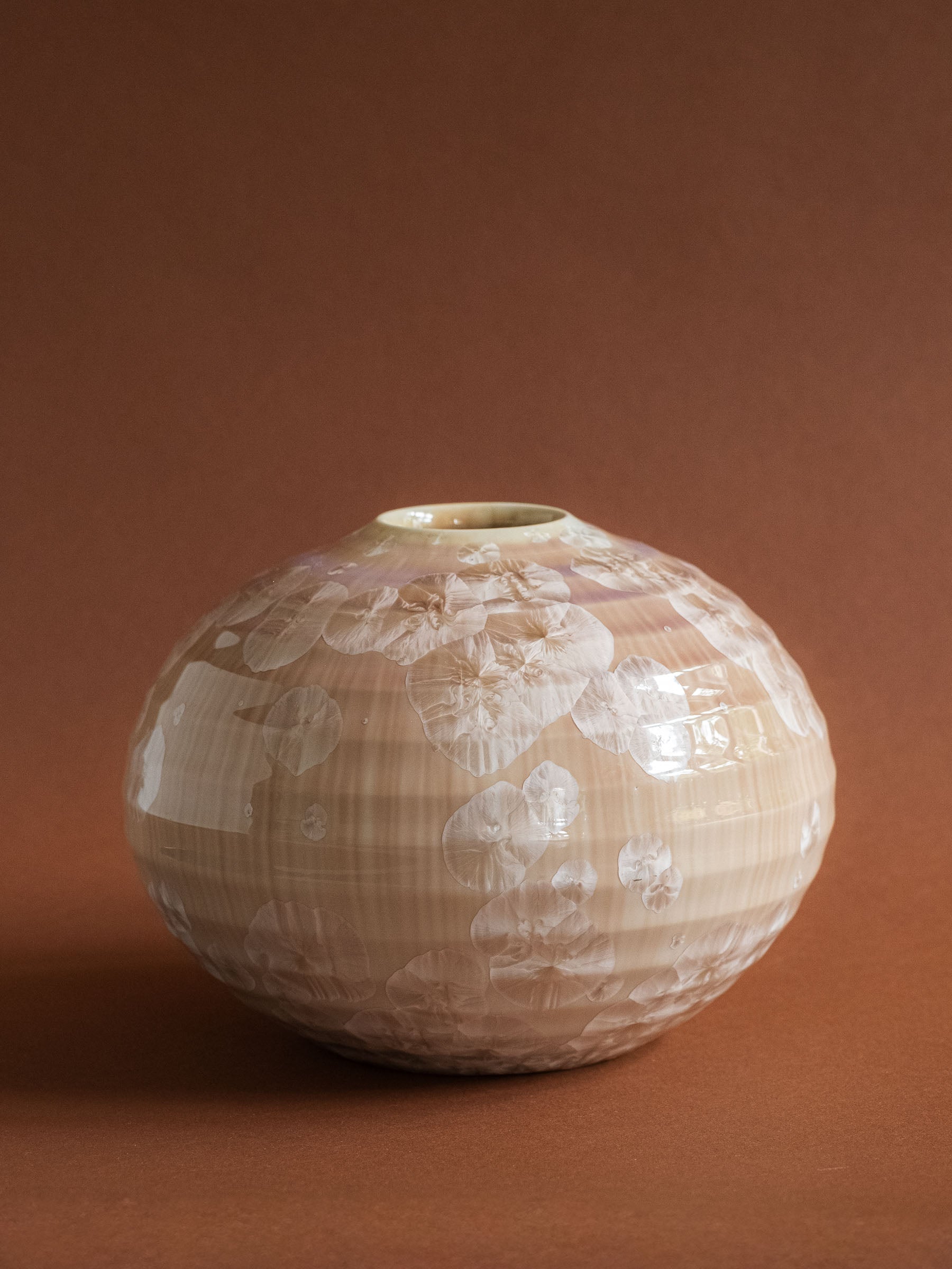 Hero view of the Japanese crystalline glaze vase against a warm reddish background, showing its broad low body and luminous crystal pattern.