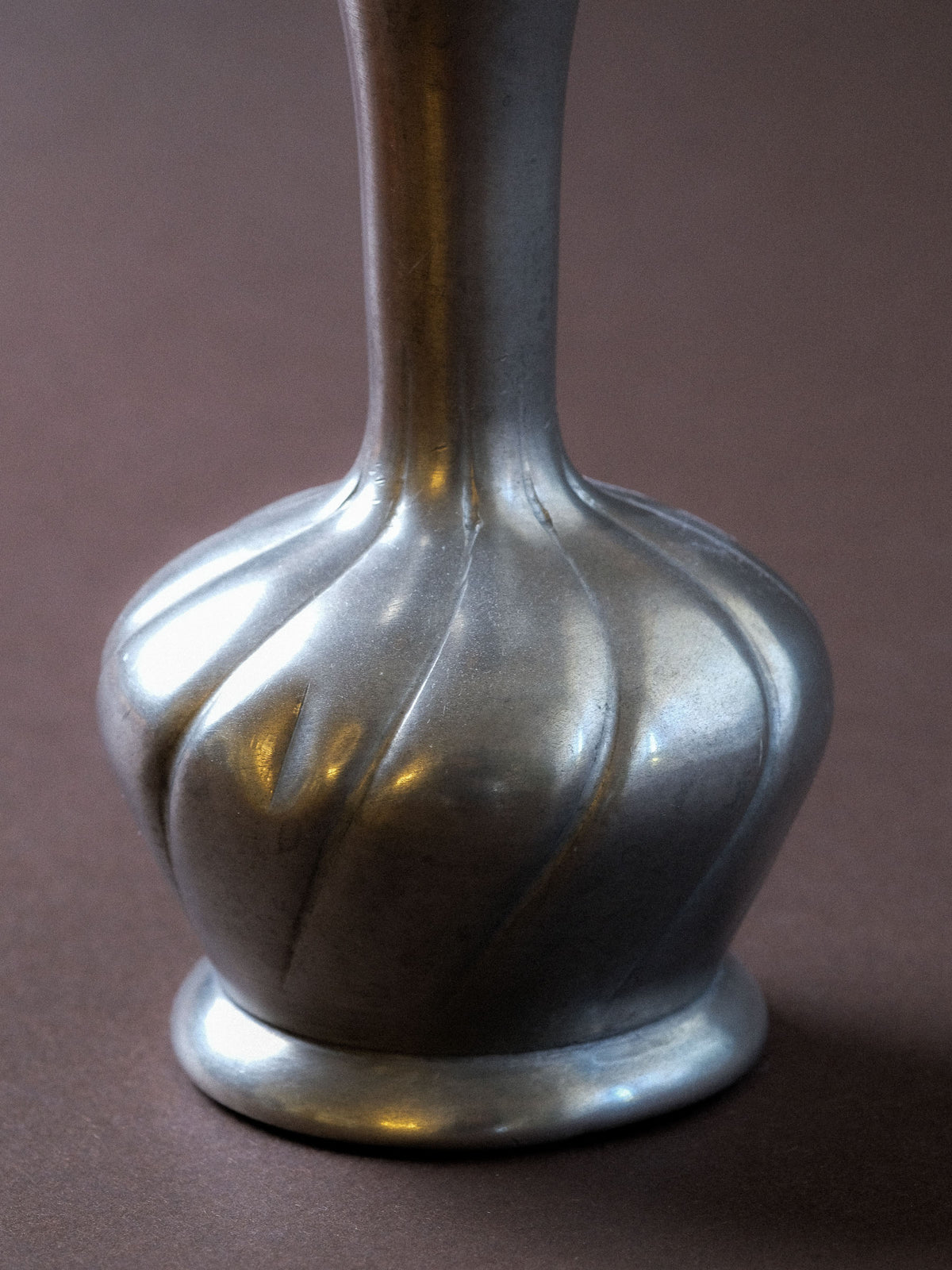 Close-up of the rounded lower body of the 95% pewter vase showing the deep spiral fluting and soft metallic surface.