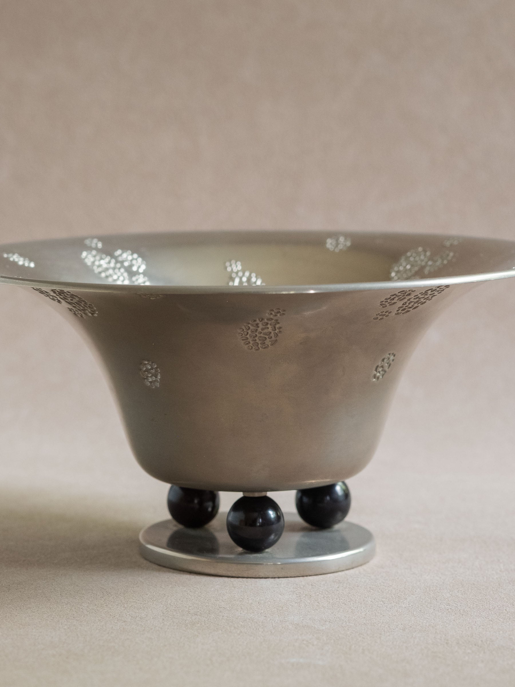 Close front view of a silver-toned WMF metal pedestal tazza bowl with black ball feet and raised dotted decoration.