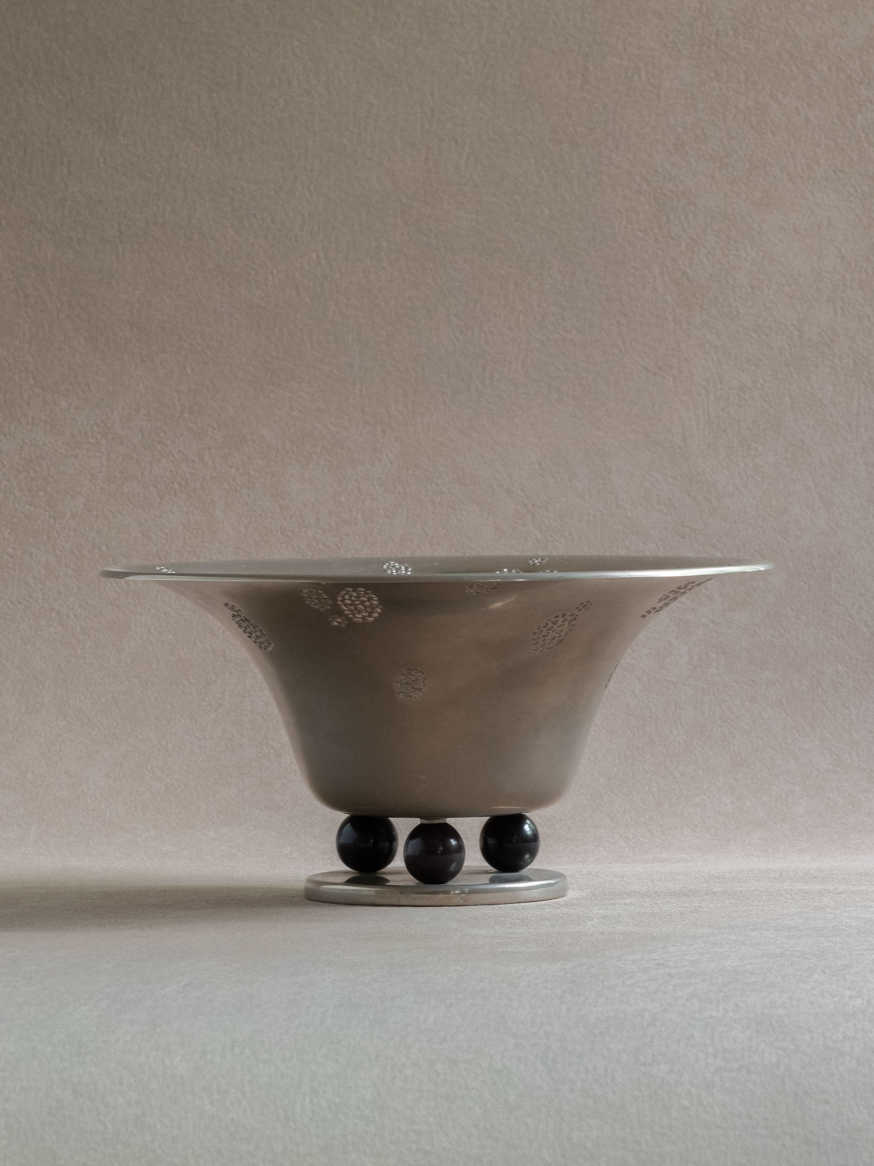 Front view of a WMF metal pedestal tazza bowl with a wide flared body, low circular base, and black spherical feet.