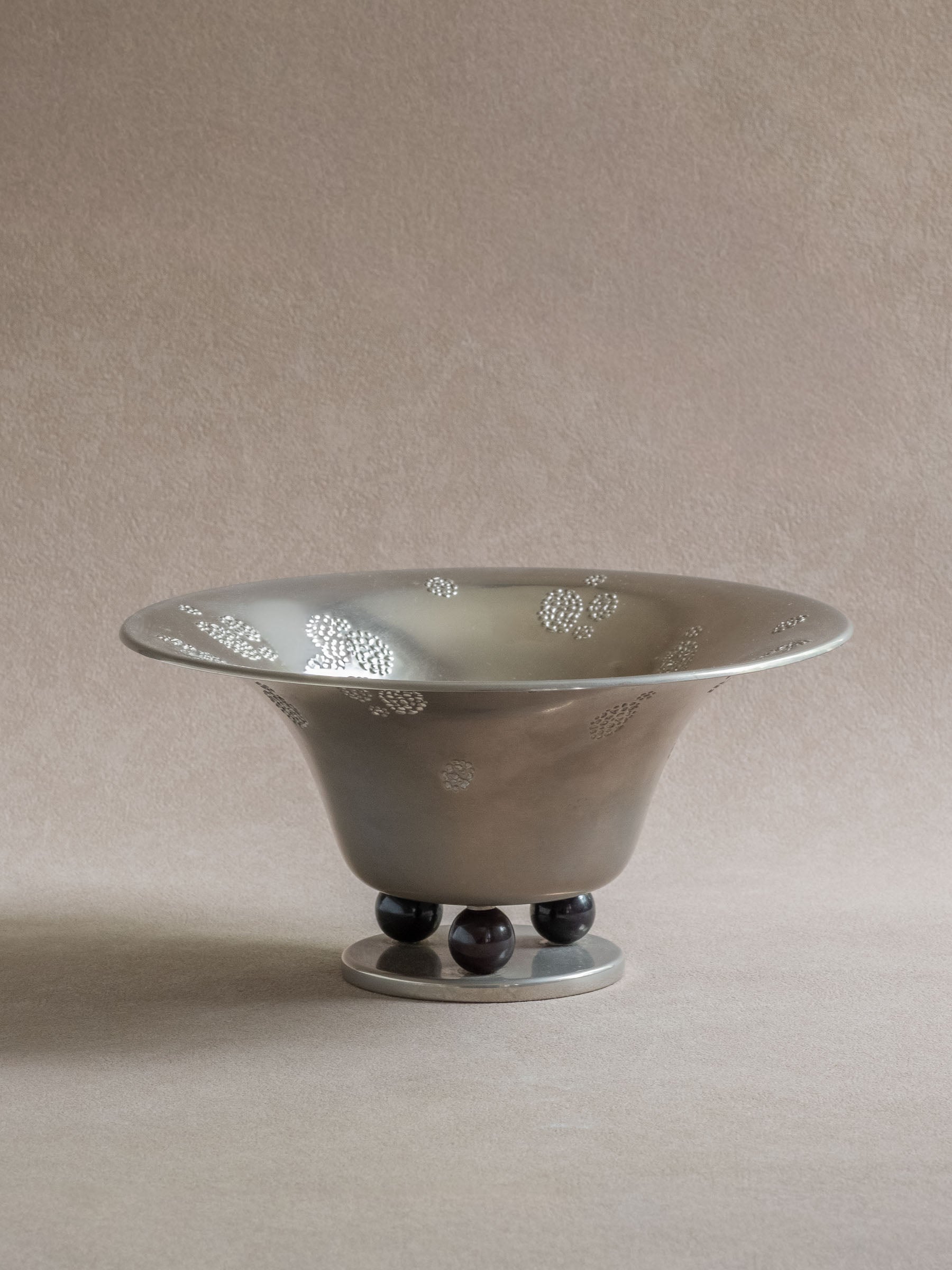 Three-quarter view of a silver-toned WMF metal pedestal tazza bowl with raised dotted decoration and black ball feet.