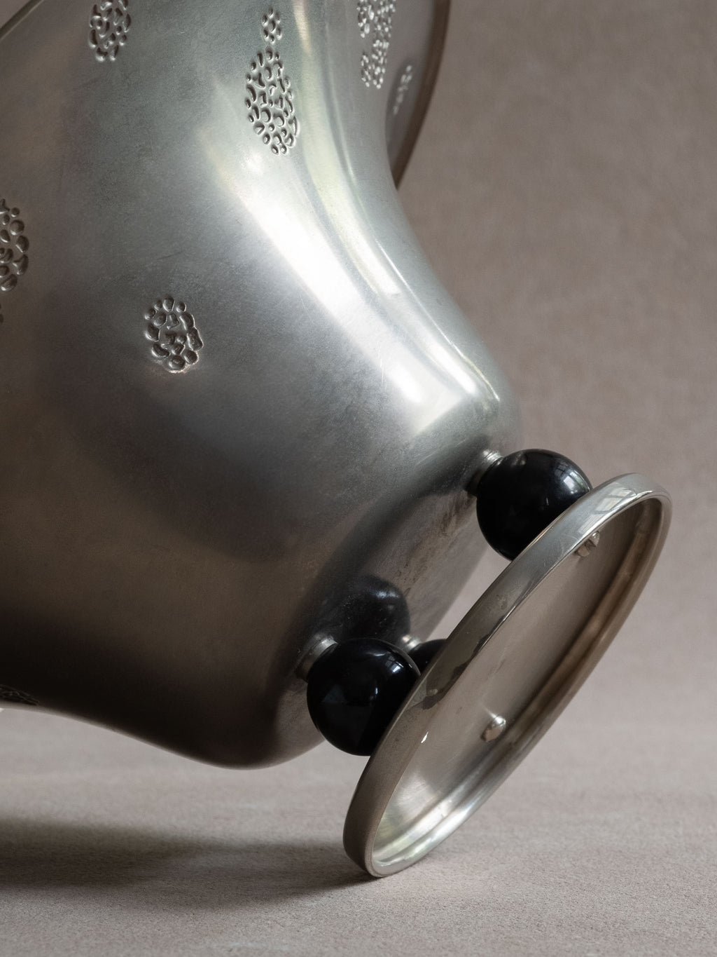 Close-up side view of a WMF metal pedestal tazza bowl showing the black spherical feet and low circular base.