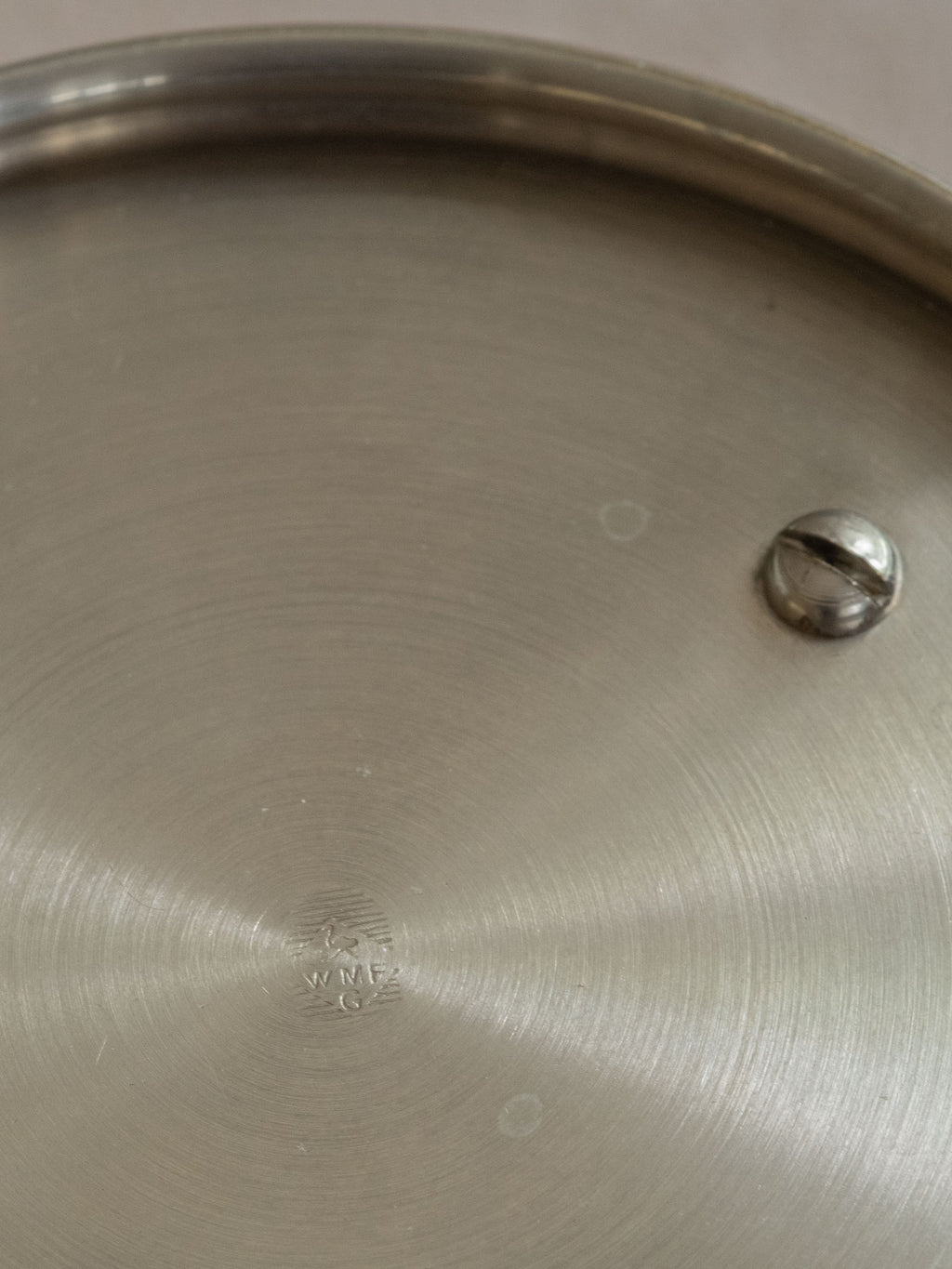 Underside detail of a WMF metal pedestal tazza bowl showing the ostrich mark and circular metal surface.