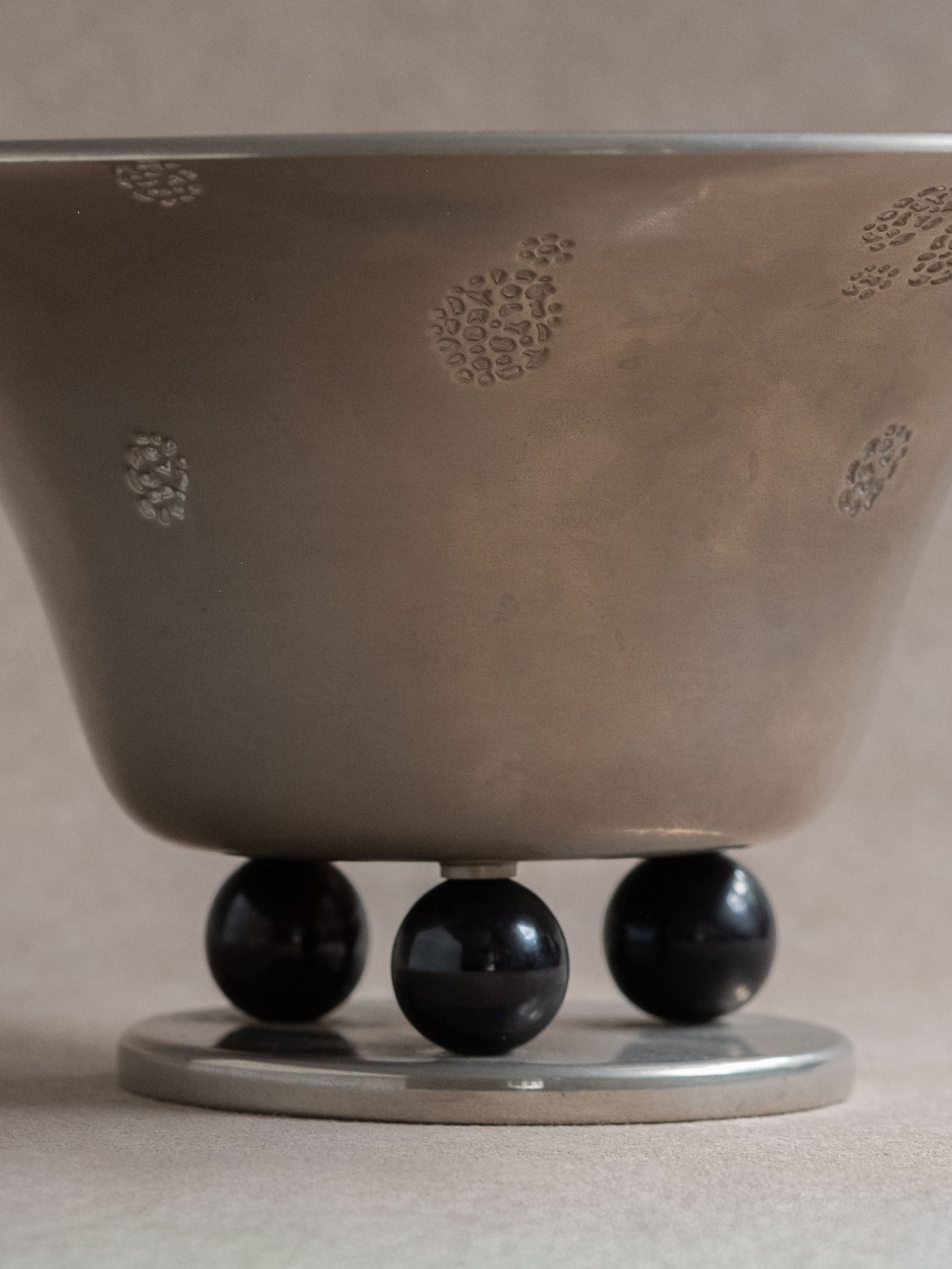 Close-up of the lower body of a WMF metal pedestal tazza bowl with three black spherical feet.