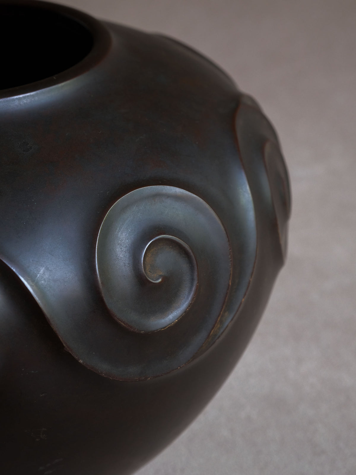 Detail of a raised spiral motif projecting from the substantial rounded bronze body.